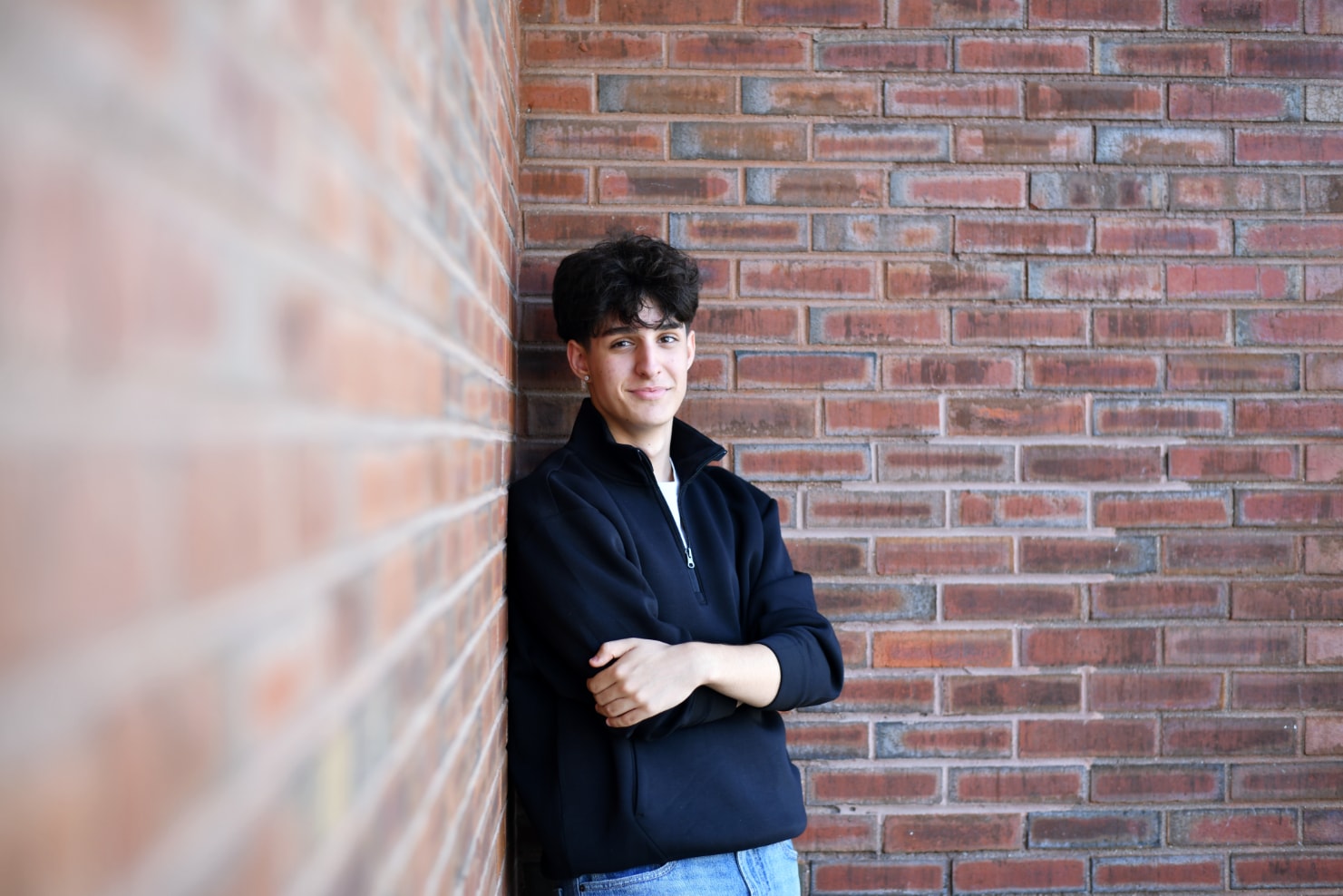 Senior portrait of young man leaning against brick wall arms crossed
