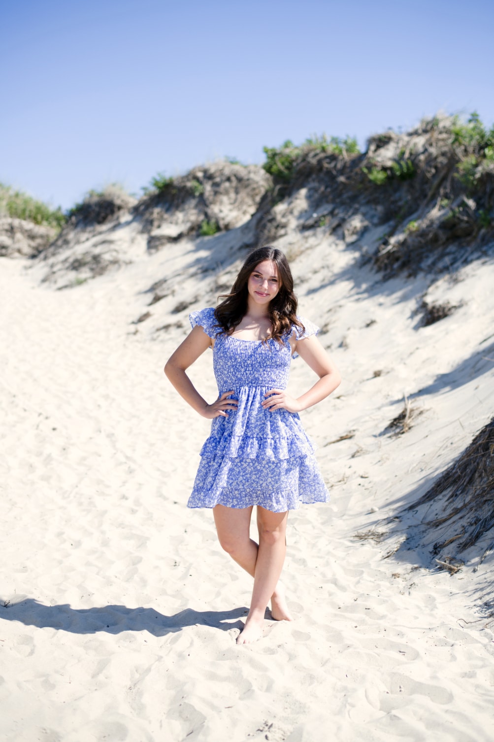 Senior portrait of young woman in blue floral dress standing on sand dunes