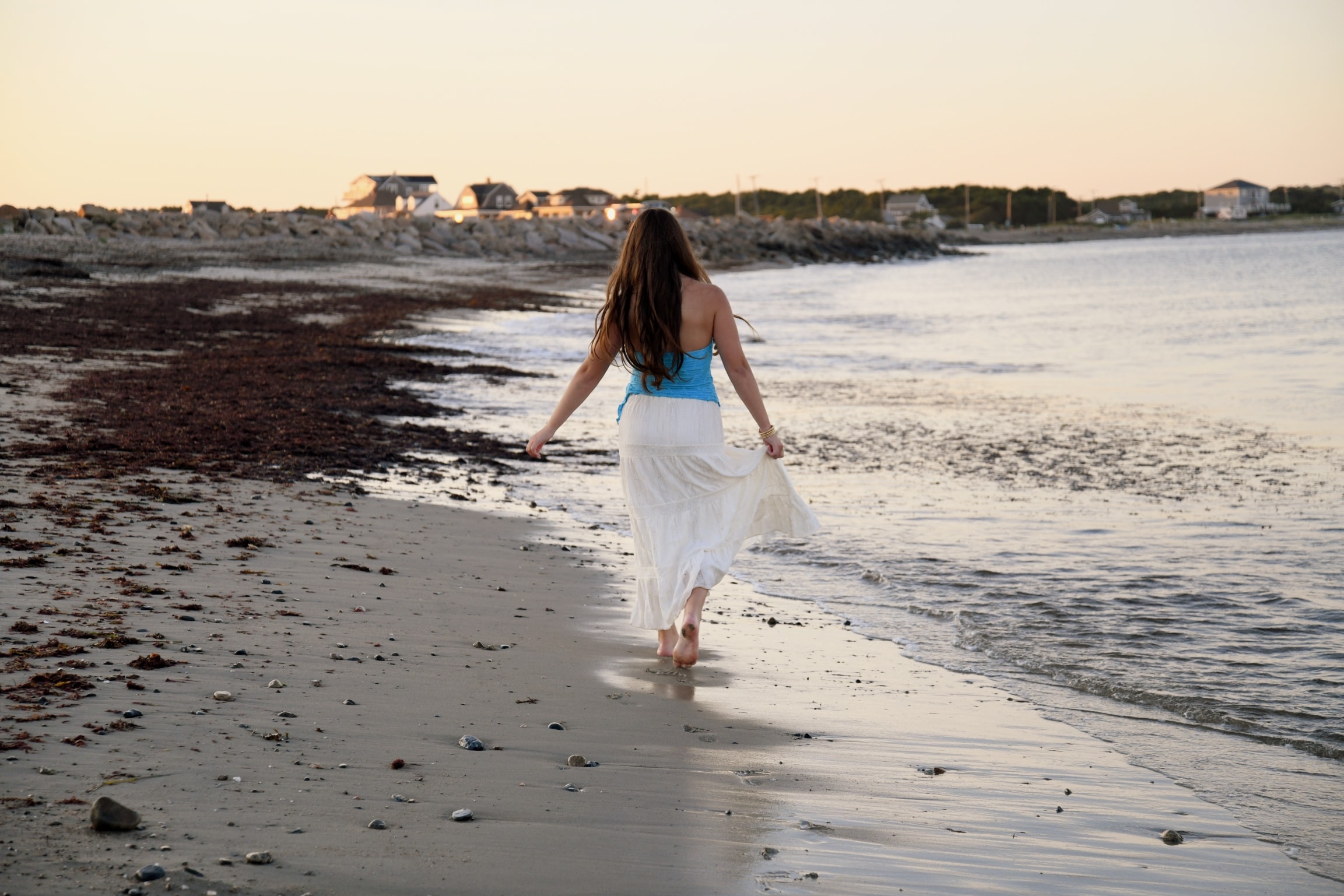 Senior portrait of young woman walking along shoreline at sunset