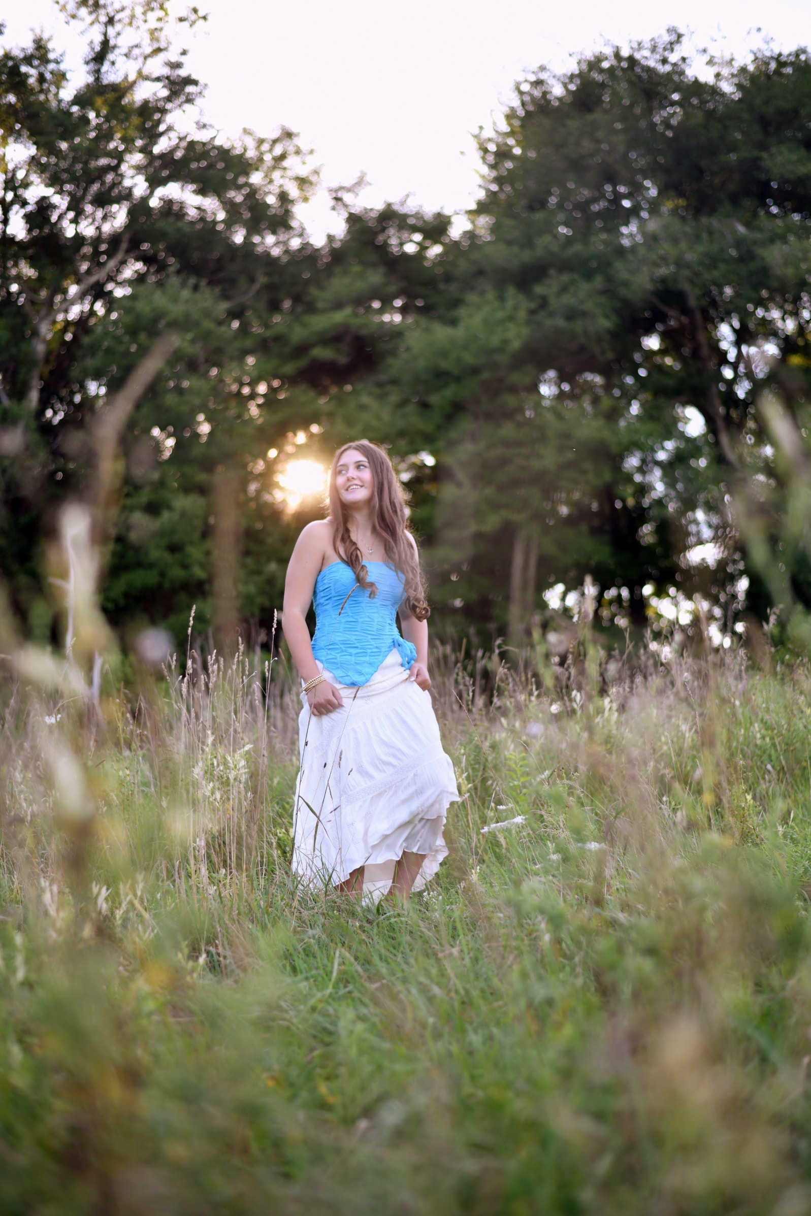 Senior portrait of young woman standing in golden meadow at sunset