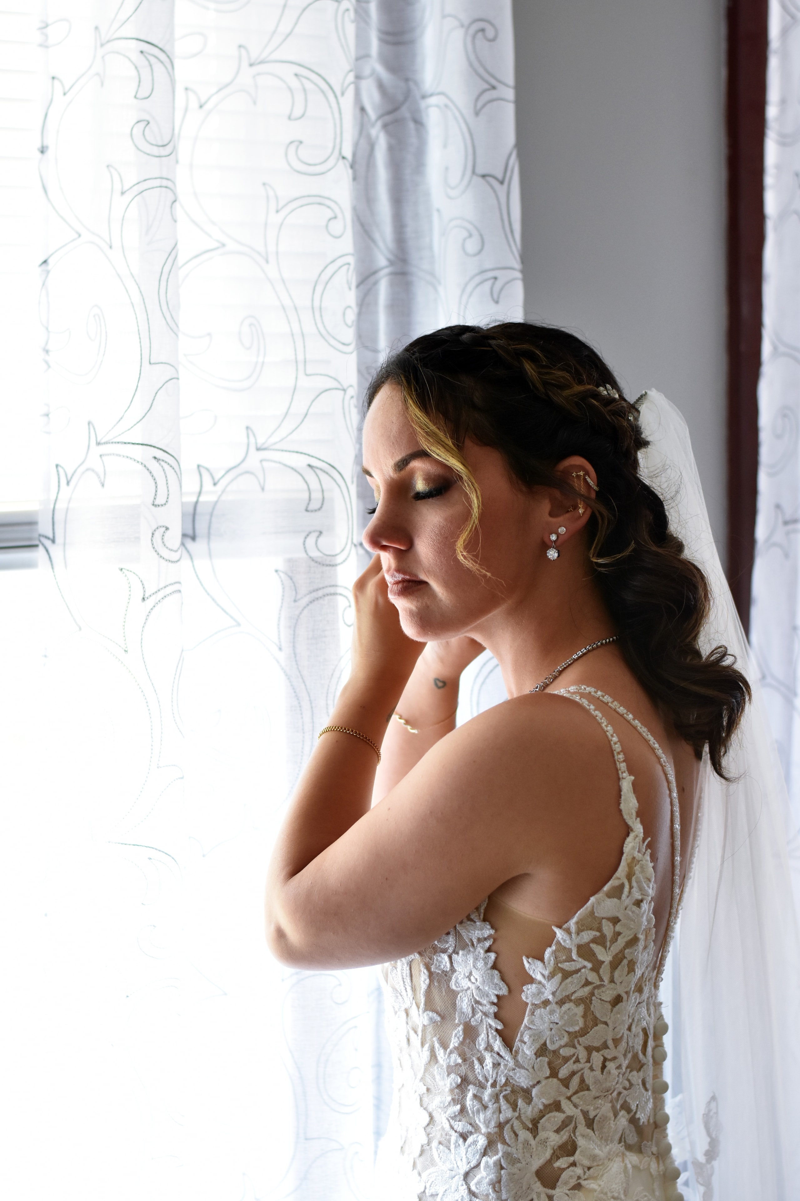 Bride getting ready by window in wedding dress