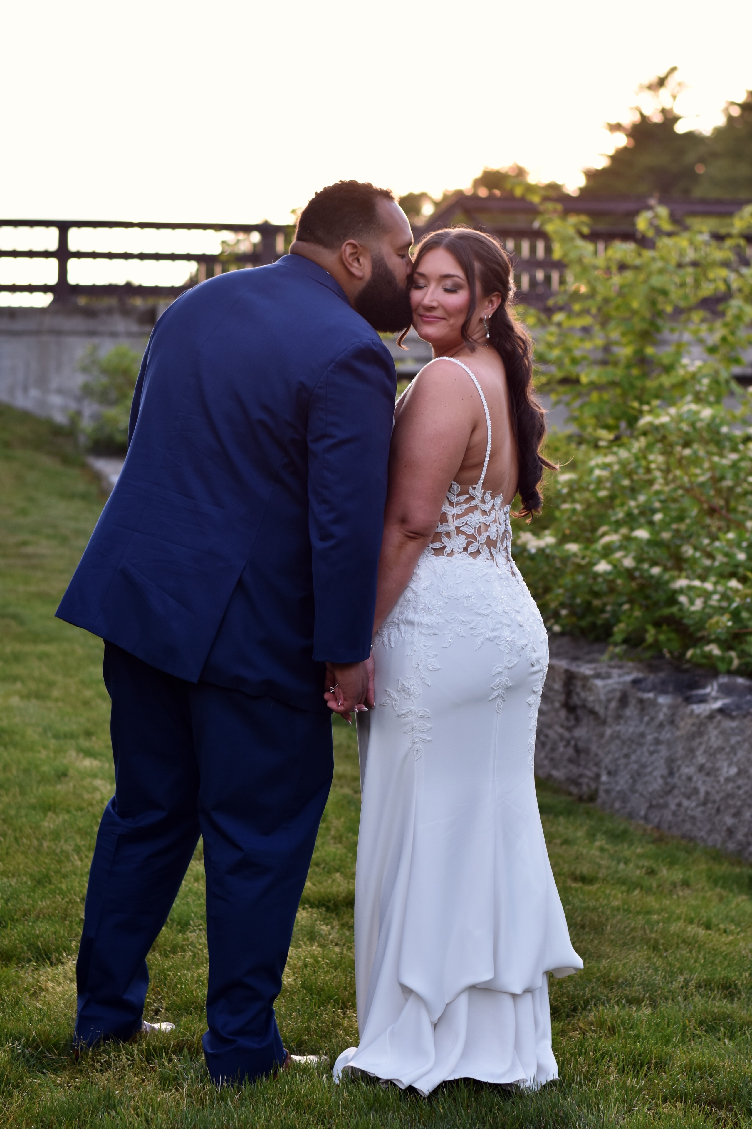 Groom kissing bride on cheek at sunset outdoors