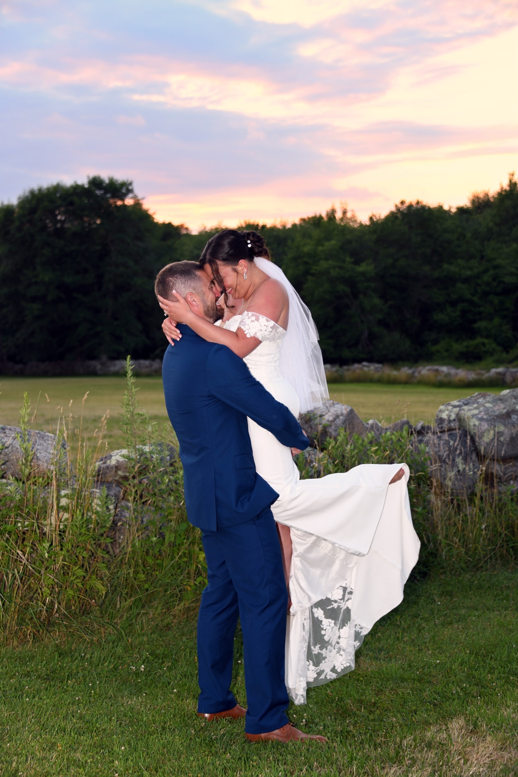 Groom lifting bride at sunset with pink and purple sky