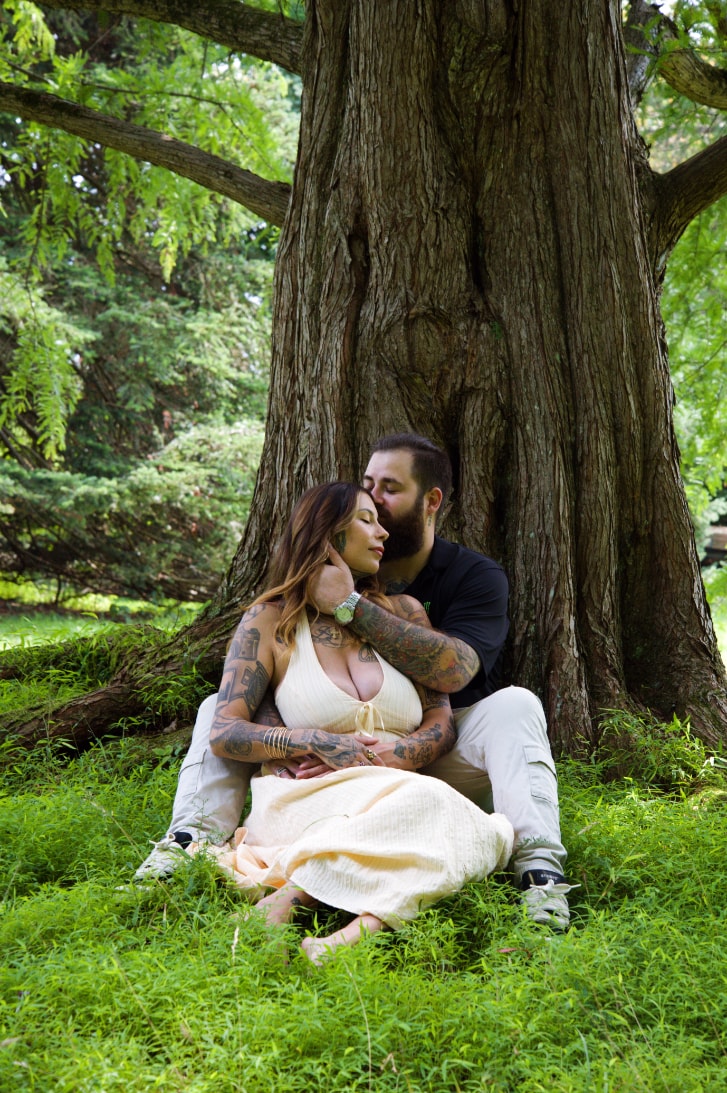 Couple sitting together against a large tree in a garden