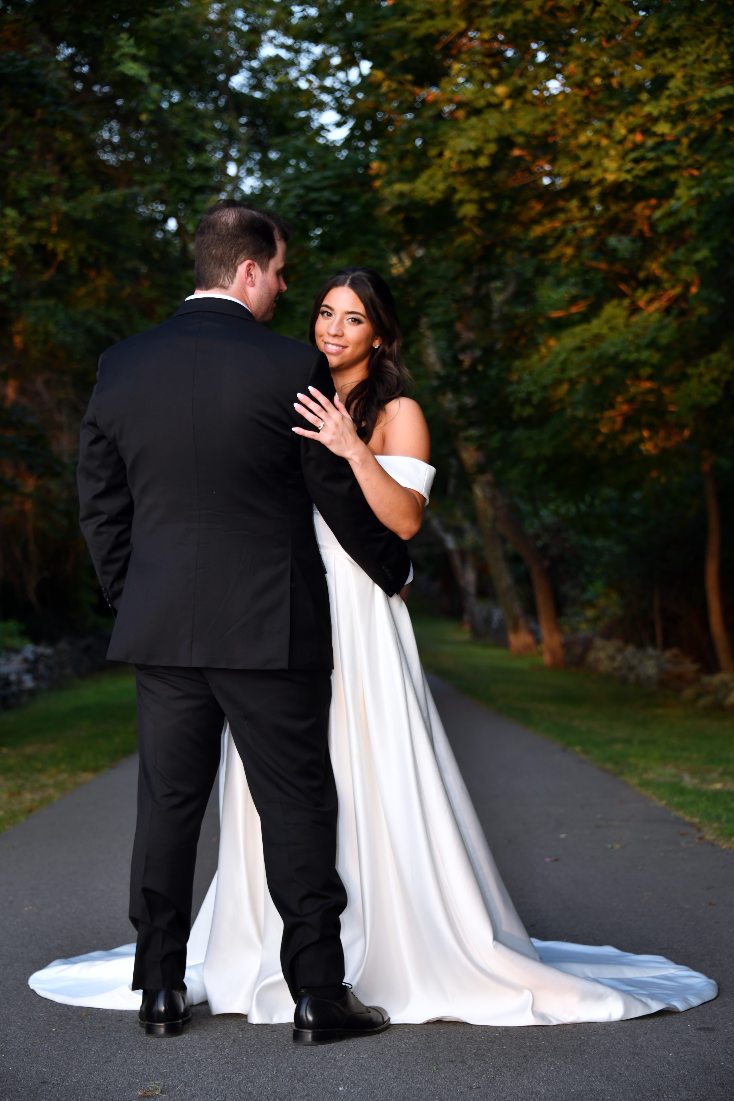 Bride smiling over groom's shoulder on tree-lined path in autumn