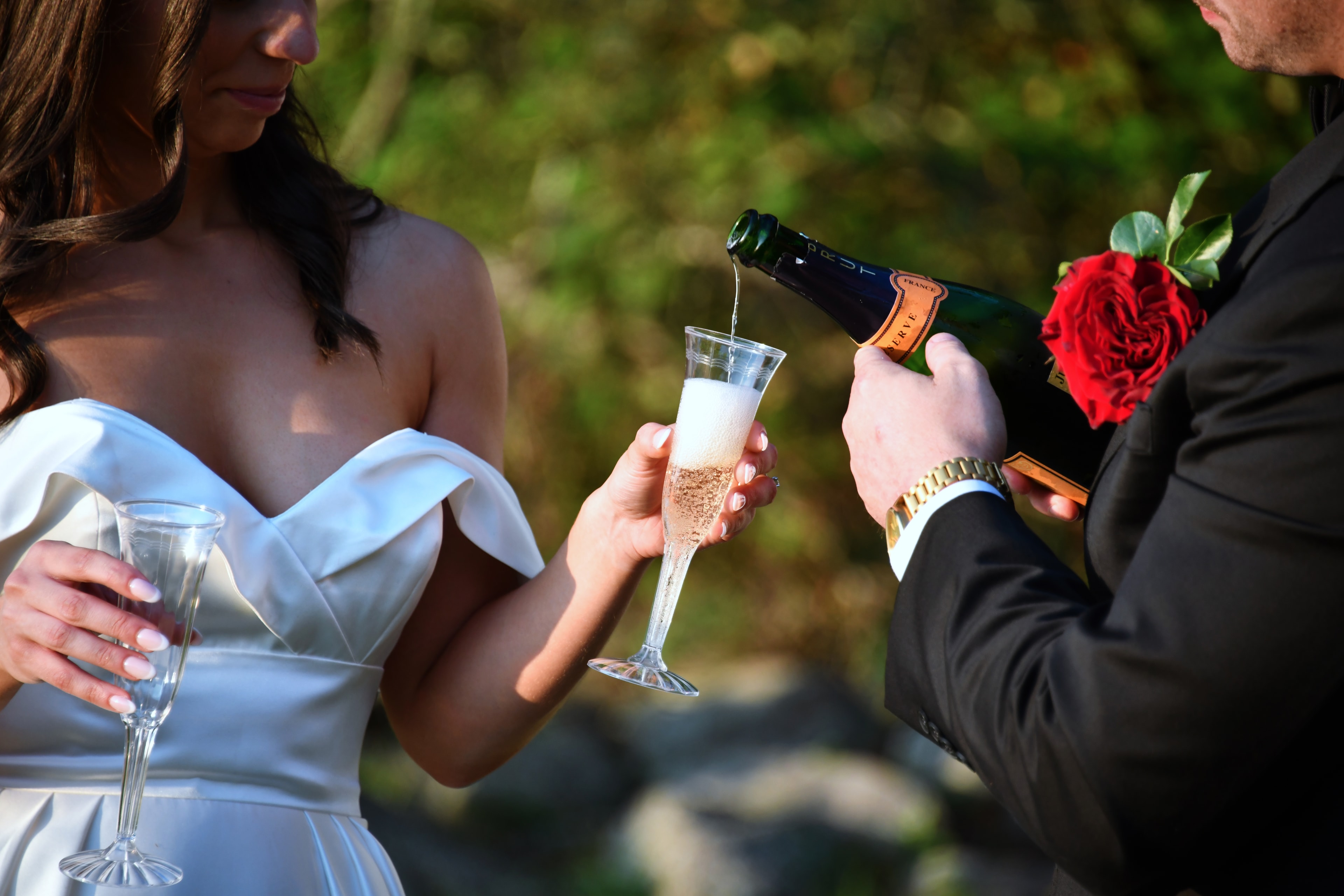 Groom pouring champagne for bride outdoors