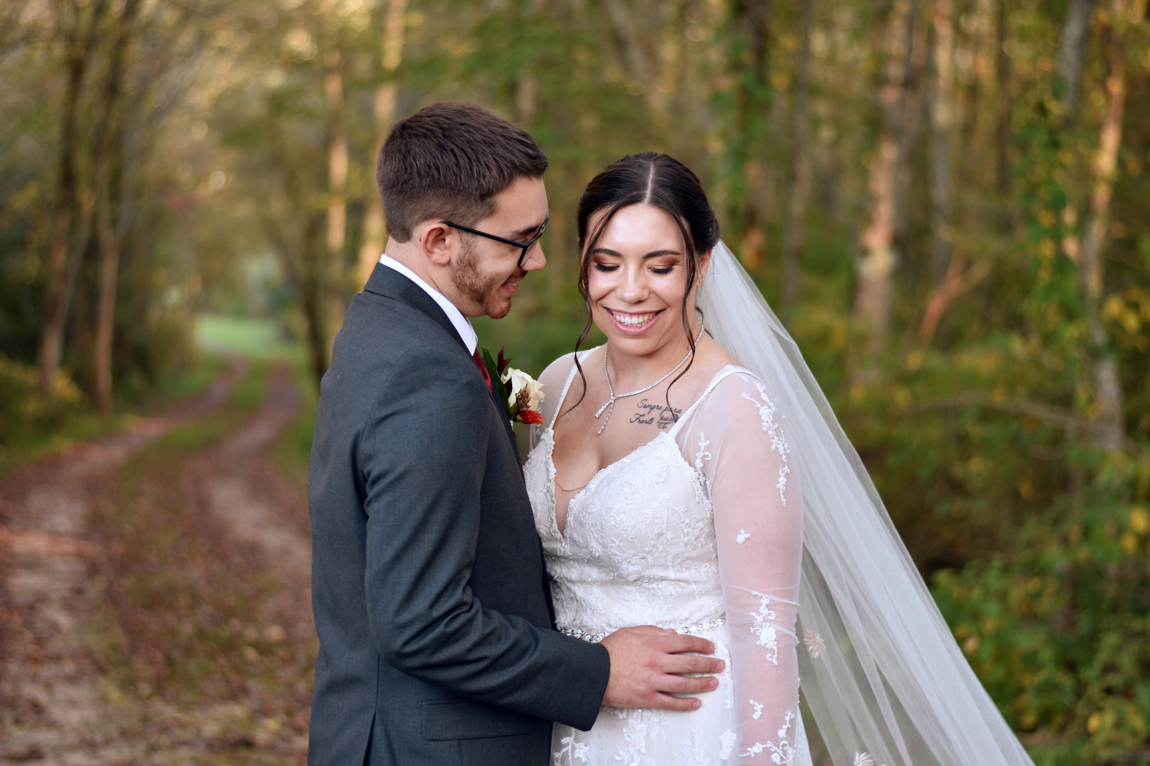 Bride and groom smiling together on wooded path in autumn
