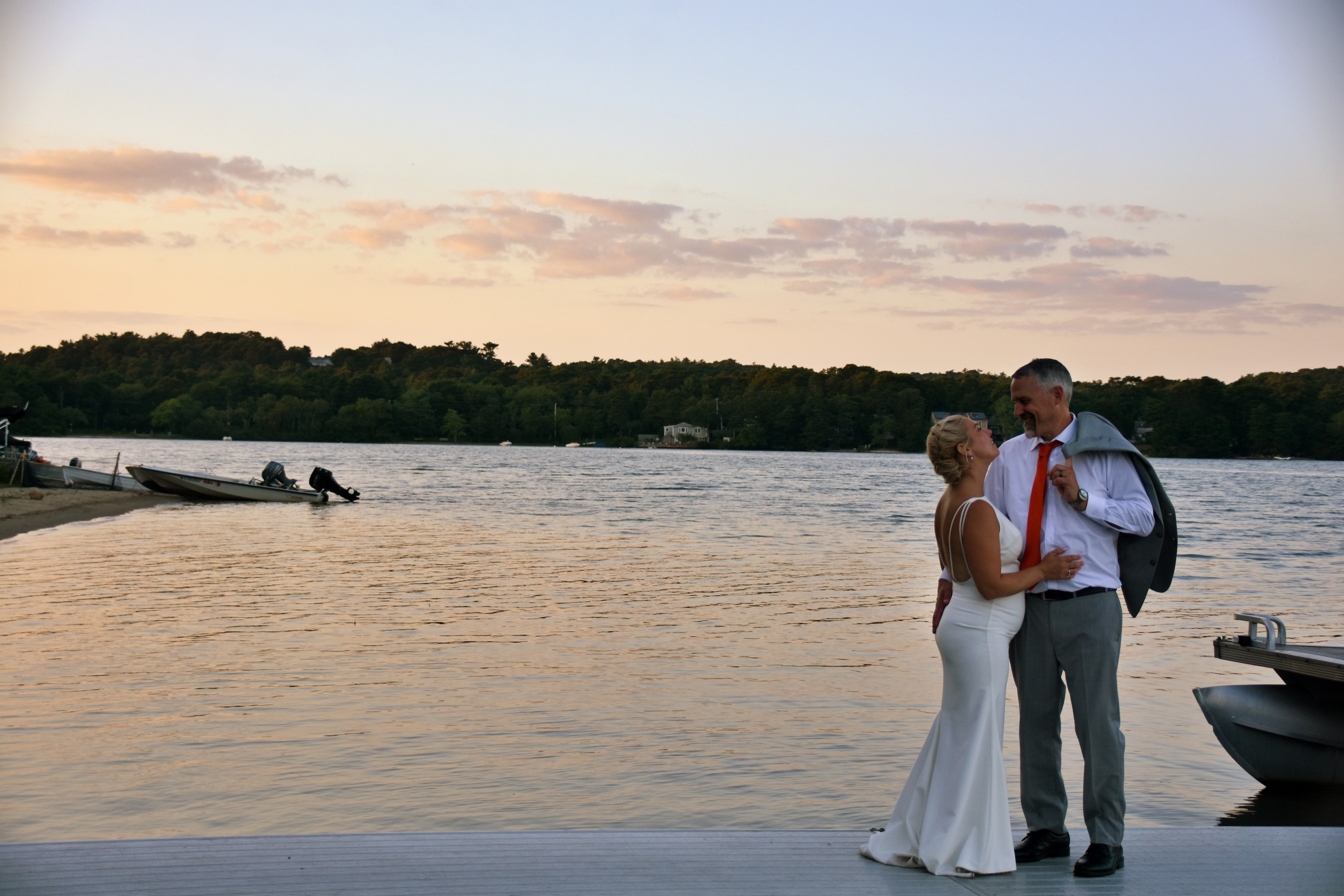 Bride and groom laughing together on dock at sunset