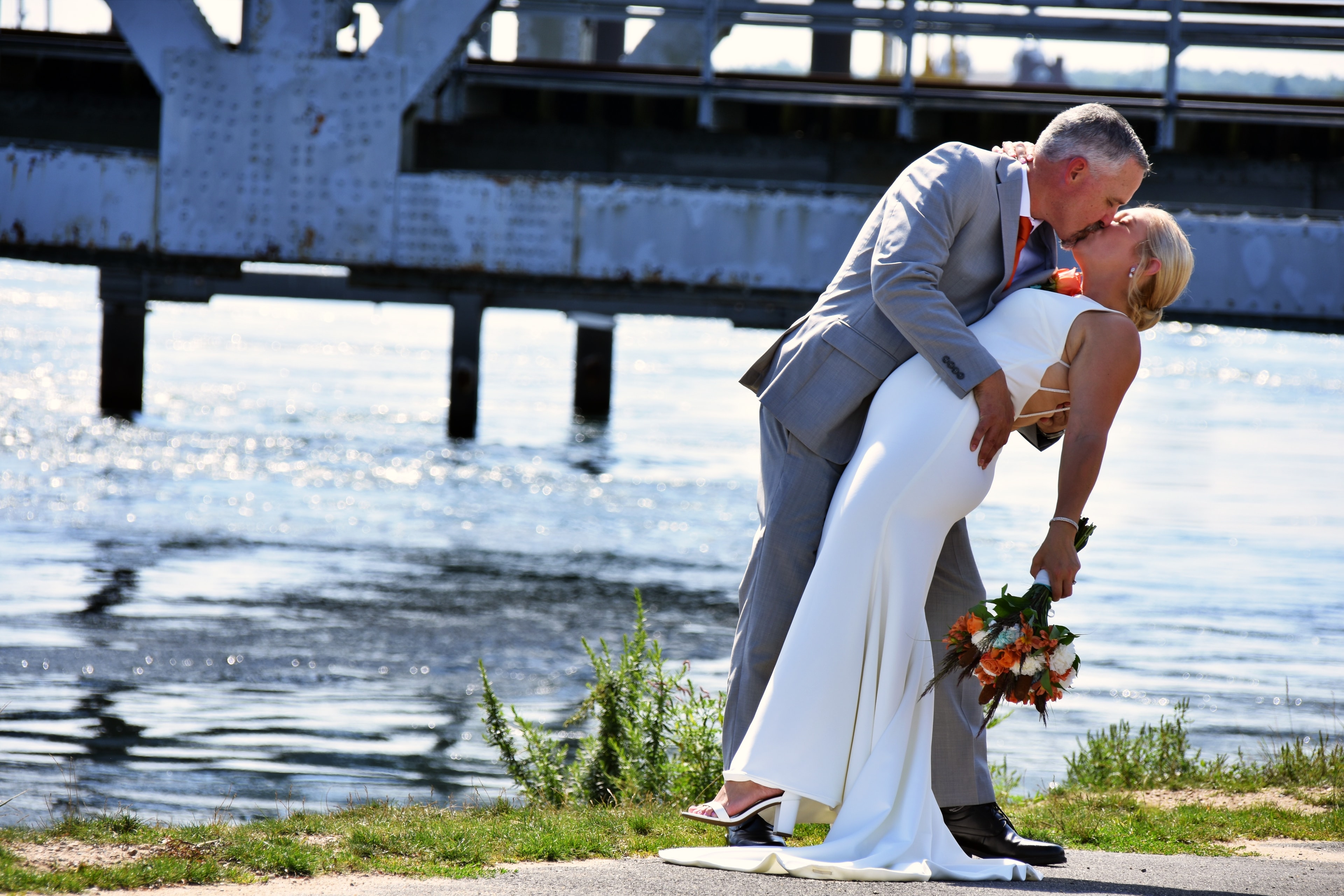 Groom dipping bride near waterfront bridge