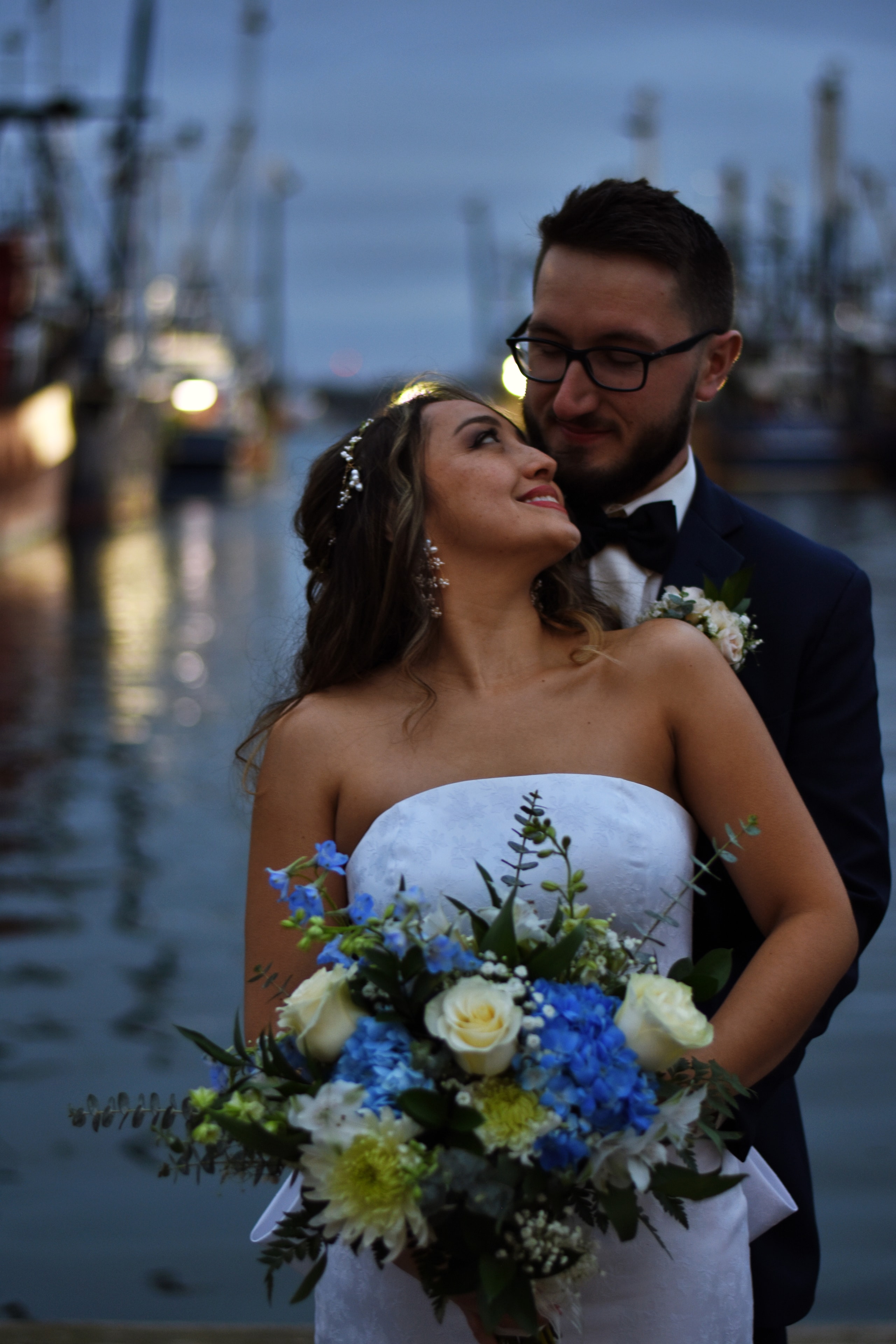 Bride and groom at dusk by the harbor with blue bouquet