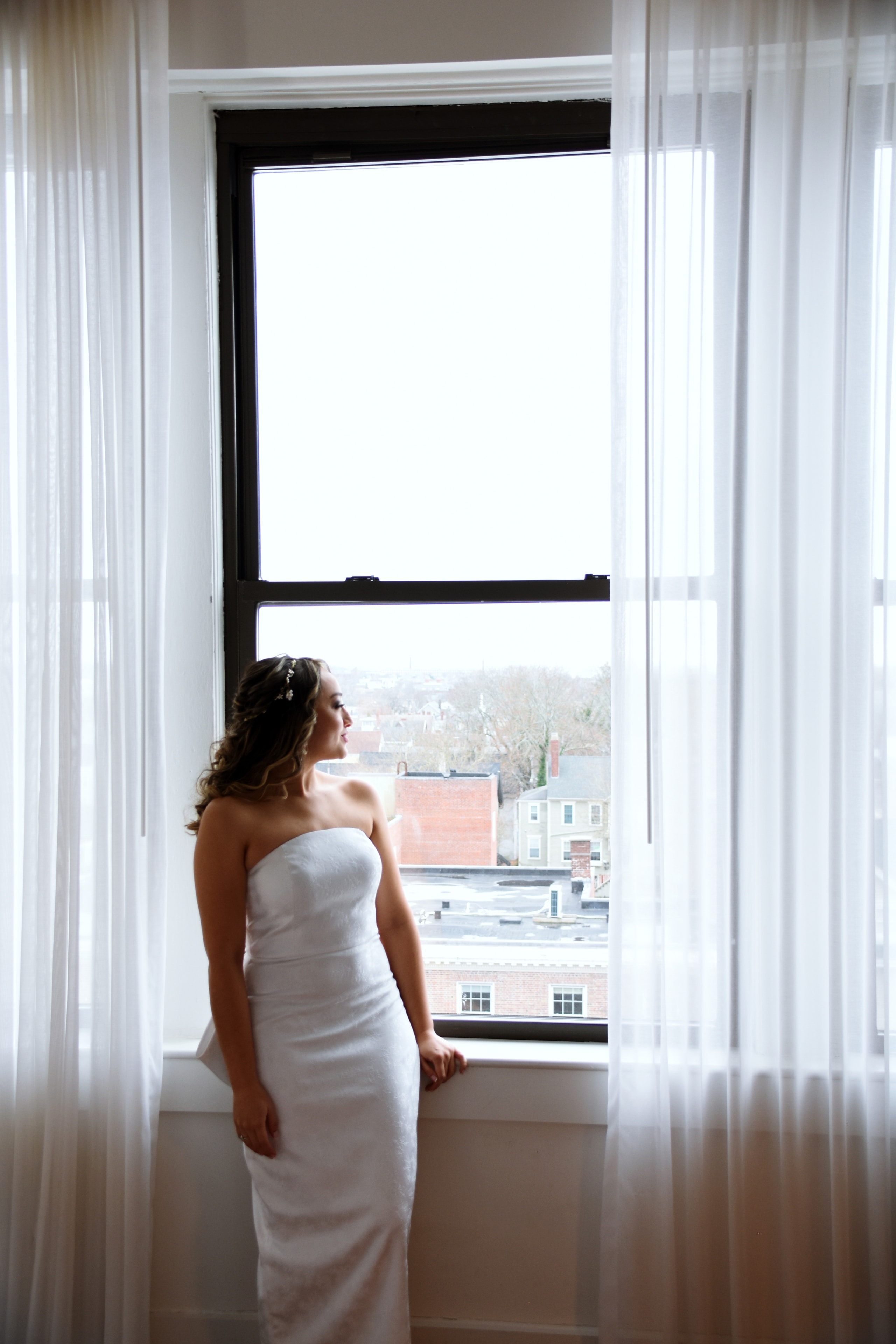 Bride in white gown gazing out tall window