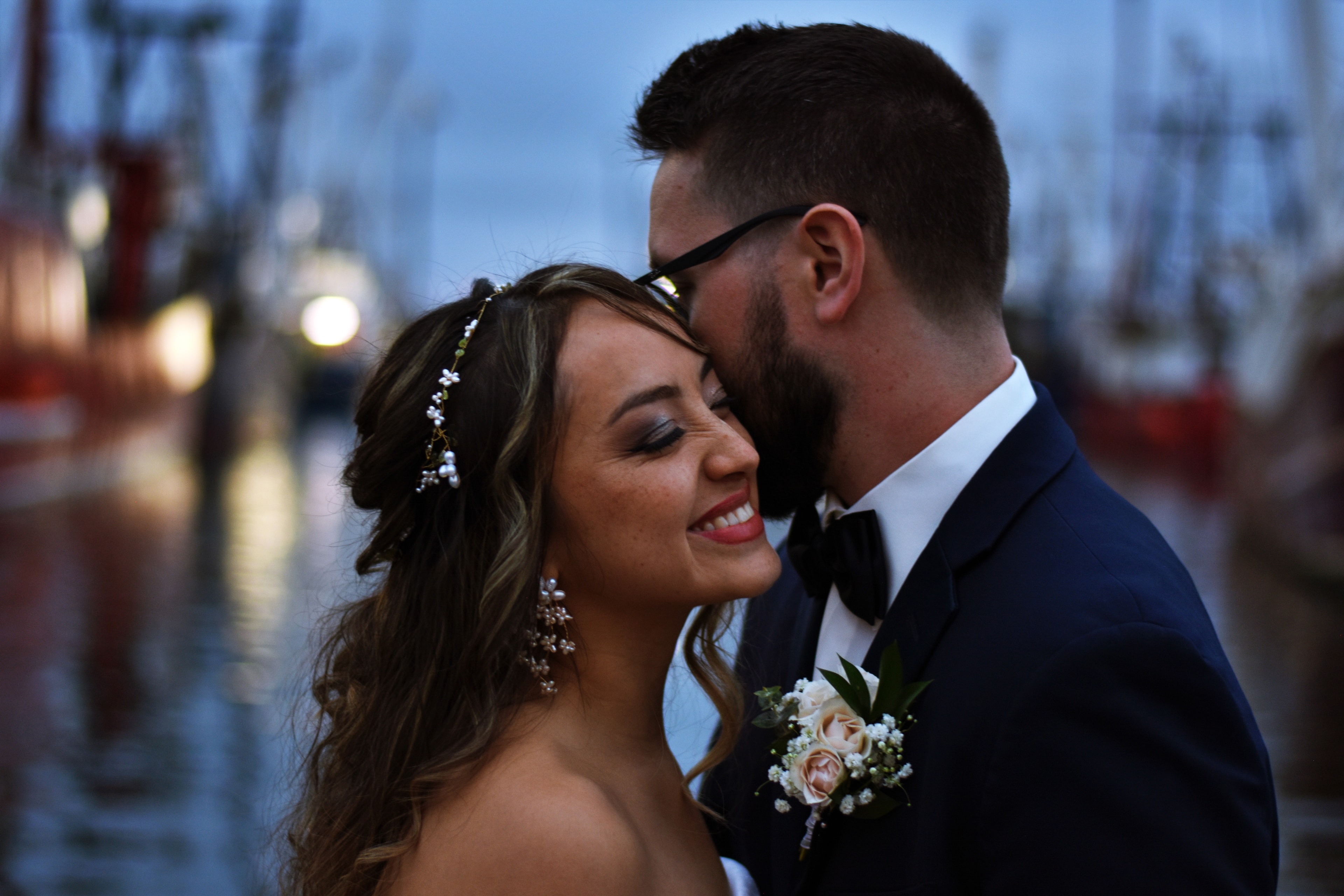 Bride smiling as groom kisses her cheek at the harbor