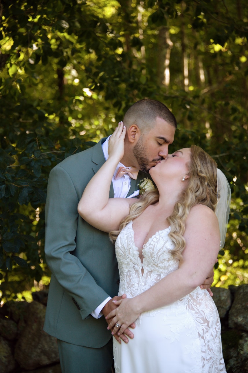 Bride and groom kissing in lush garden against stone wall