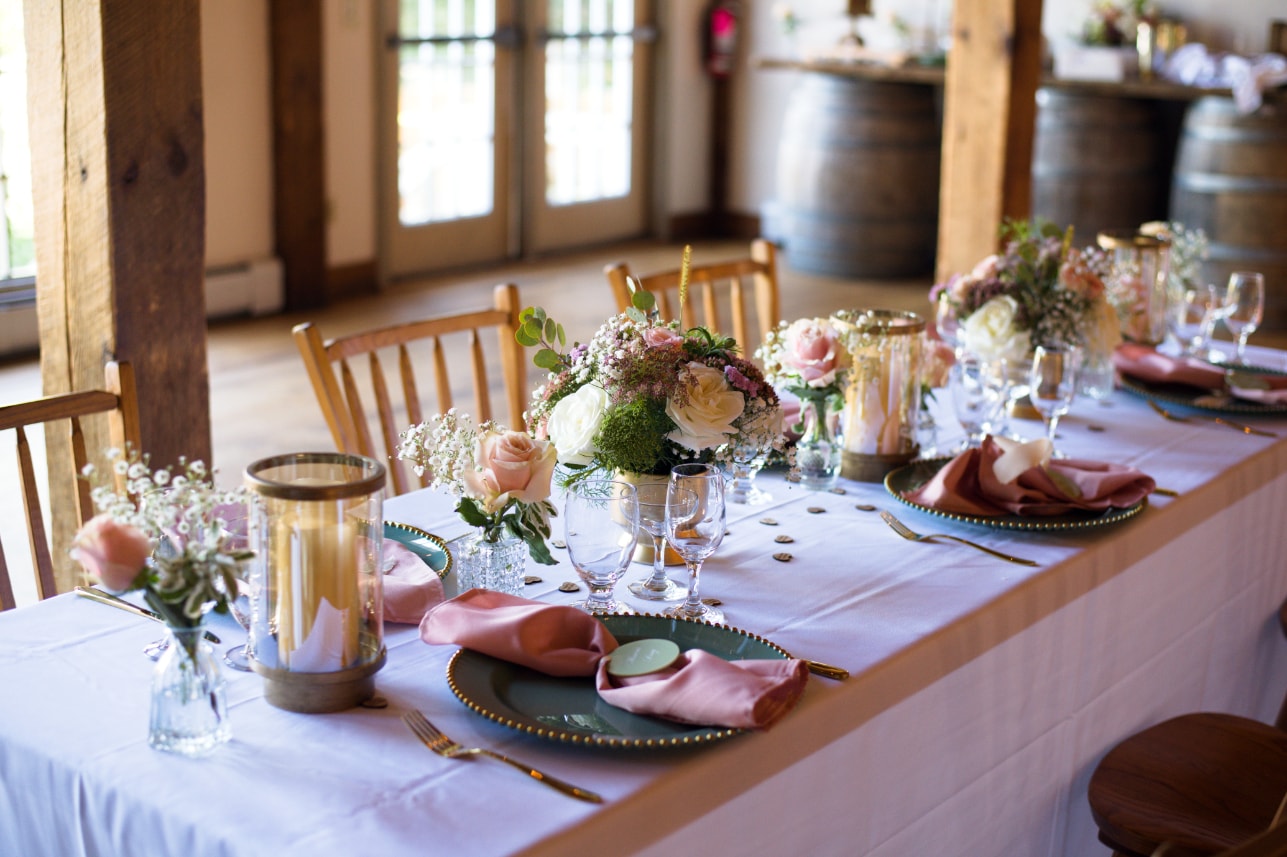 Elegant barn wedding reception table with floral centerpieces and pink napkins