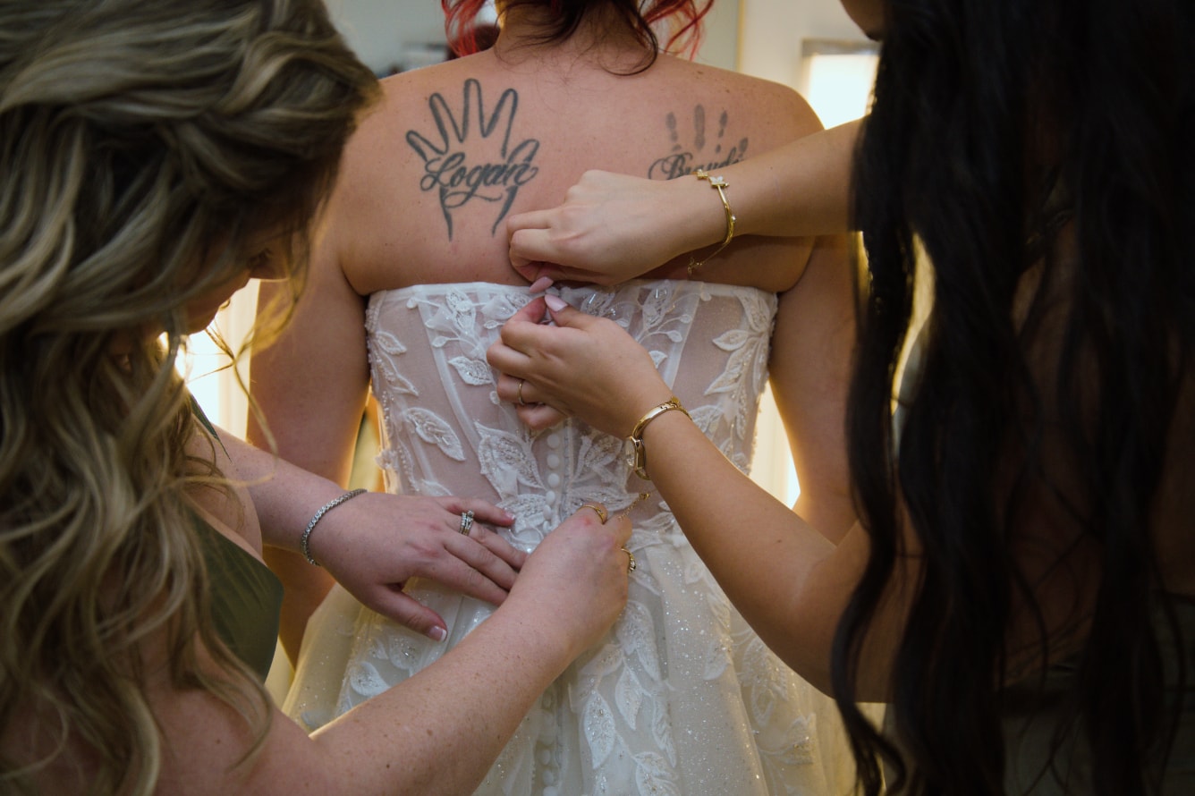 Bridesmaids helping bride button up wedding dress