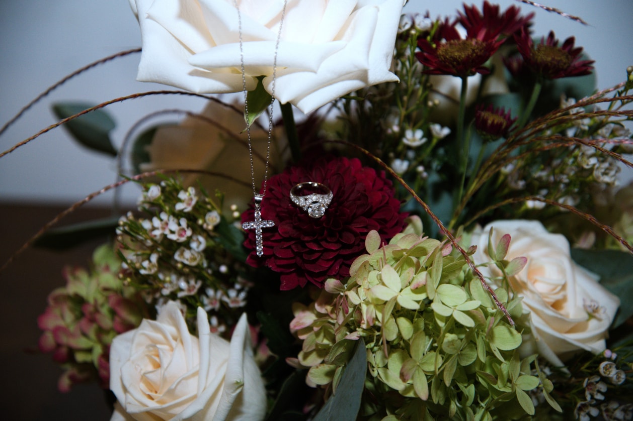 Diamond ring and cross necklace resting in burgundy and white bridal bouquet